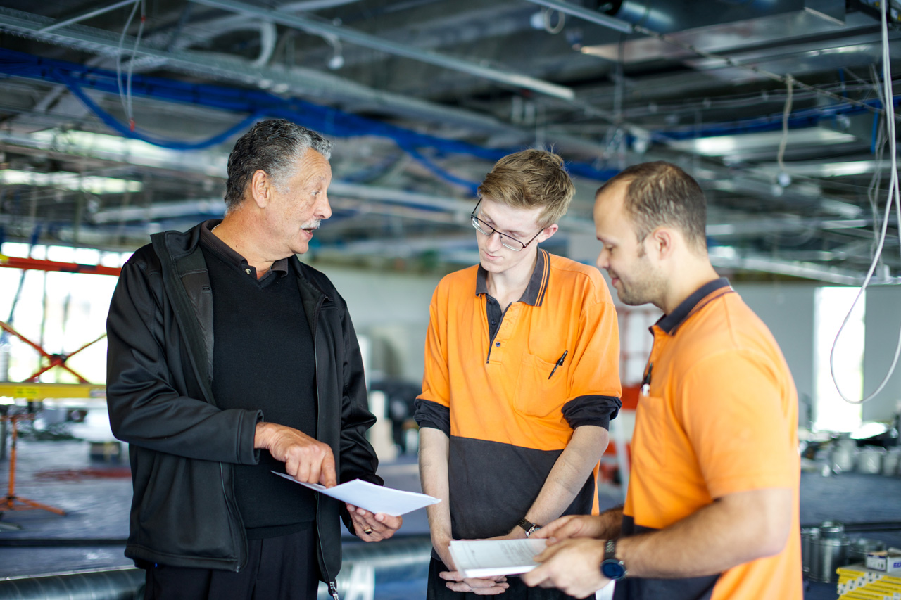 Experienced tradesman explains concepts to two apprentice electricians